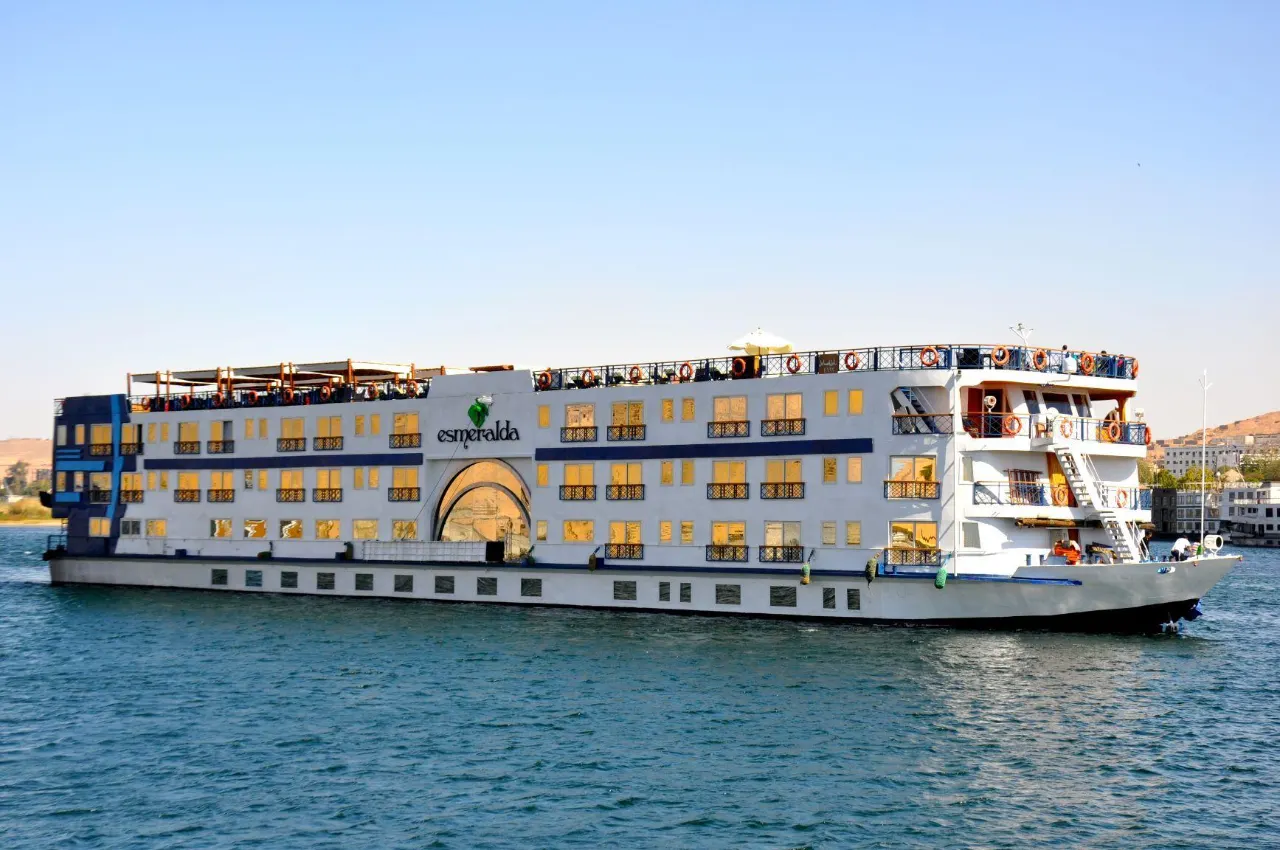 The Nile cruise ship Esmeralda under way on the Nile, desert hills and the riverbank town behind