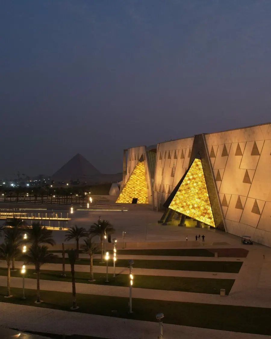 The Grand Egyptian Museum lit at dusk in Giza, the Great Pyramid on the skyline beyond
