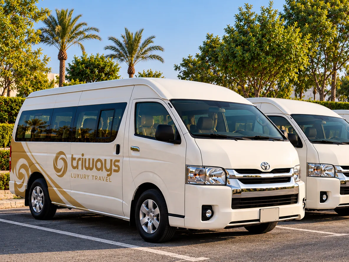 A line of white Toyota Hiace high-roof vans in Triways livery in a tree-lined car park