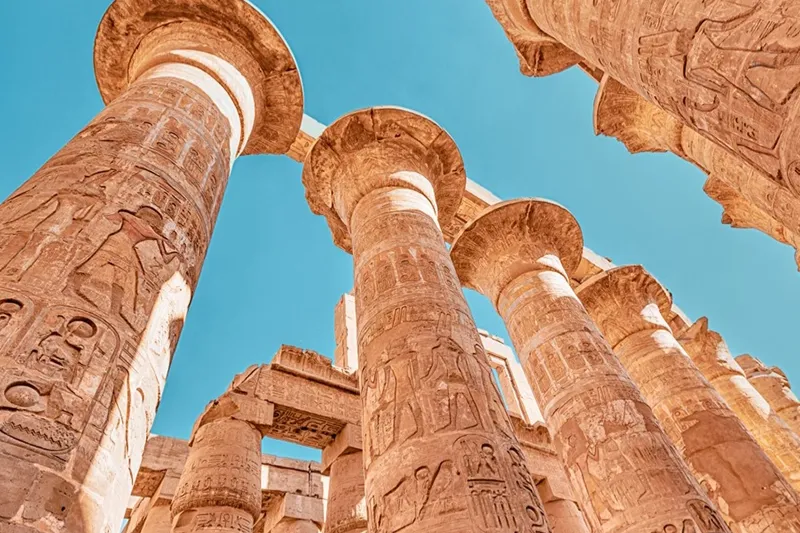 Carved columns of the Great Hypostyle Hall at Karnak against a blue sky