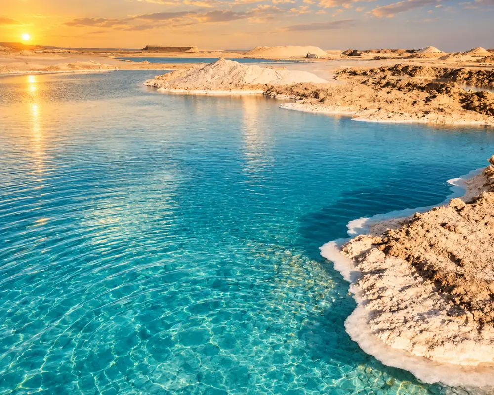 A turquoise salt lake edged with white salt crust at sunset in the Siwa oasis