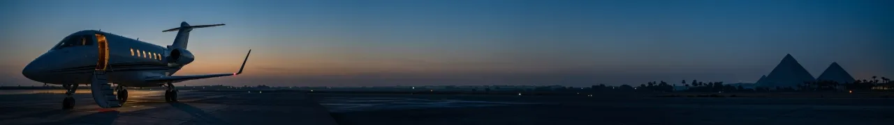A private jet with its door open on an empty apron before dawn, the silhouettes of two pyramids on the far horizon