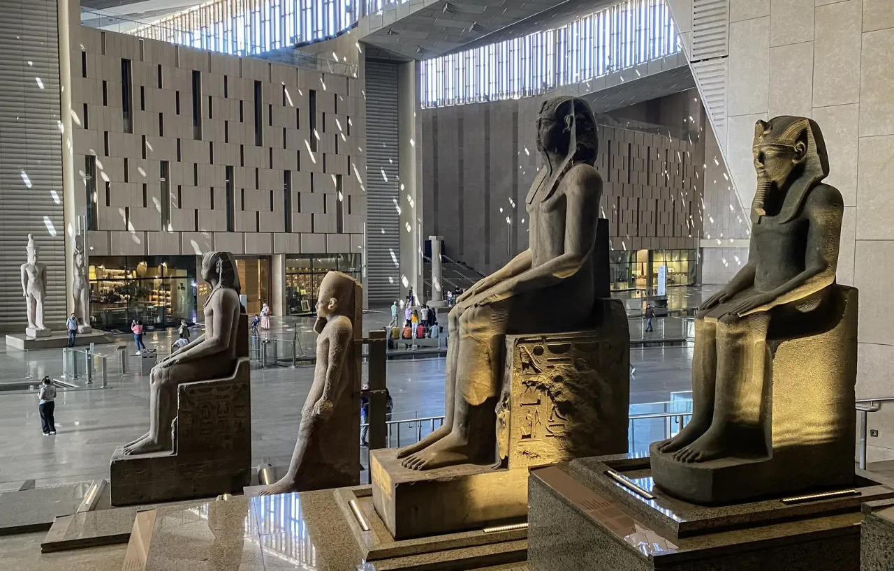Seated granite statues of pharaohs lit gold on the Grand Staircase of the Grand Egyptian Museum