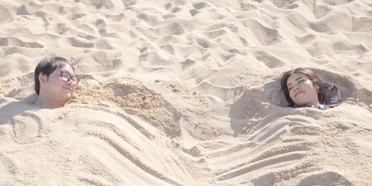 Two travellers lying buried to the shoulders in warm sand during a sand bath