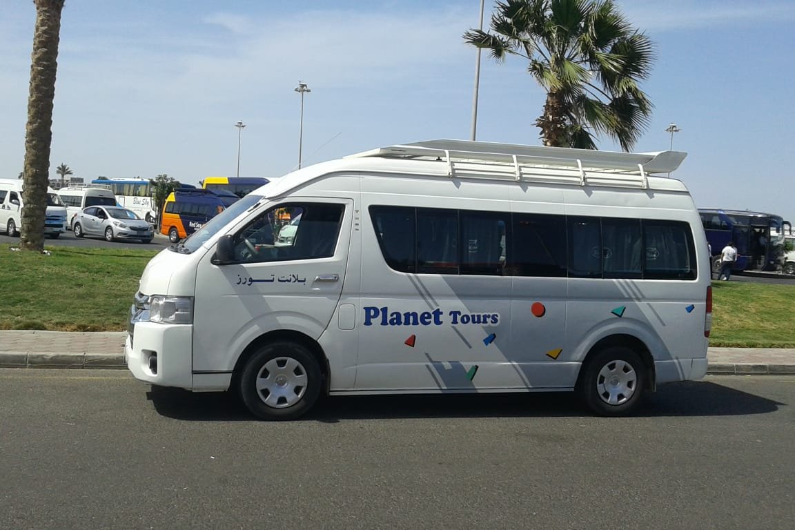 A white Toyota Hiace high-roof van on a coastal road