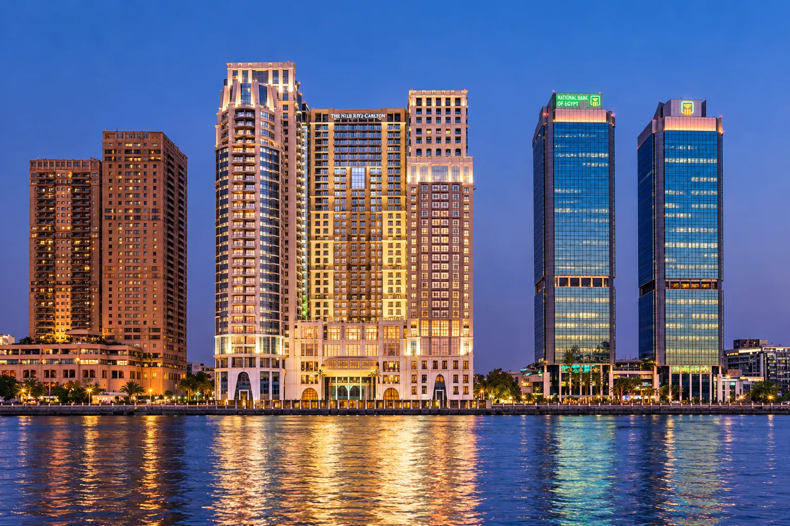 The St. Regis Cairo towers lit at dusk on the Nile corniche, reflected in the river